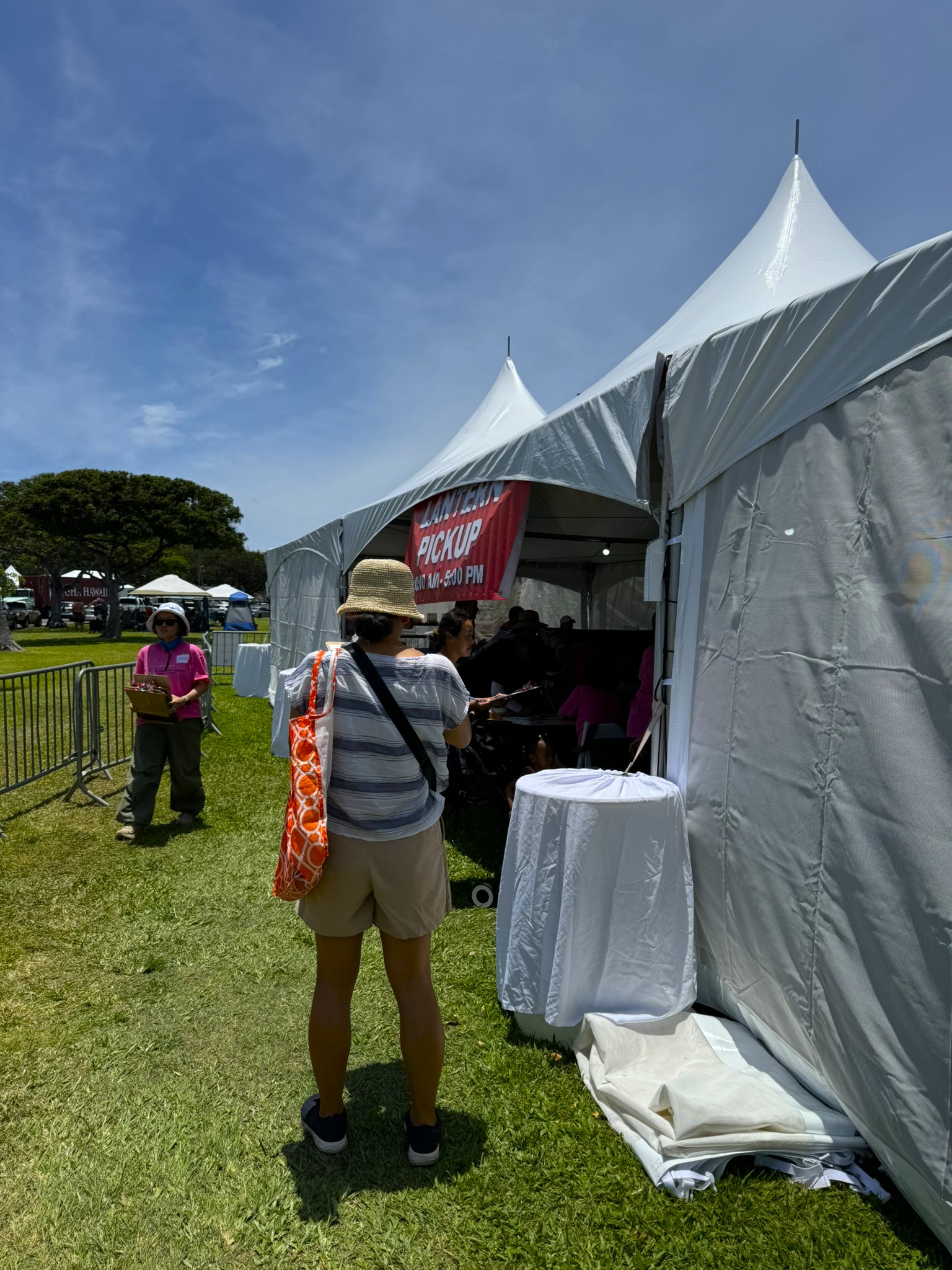 A woman in a straw hat approaching the Lantern Pickup tent, with a red 'Lantern Pickup' banner visible above the entrance
