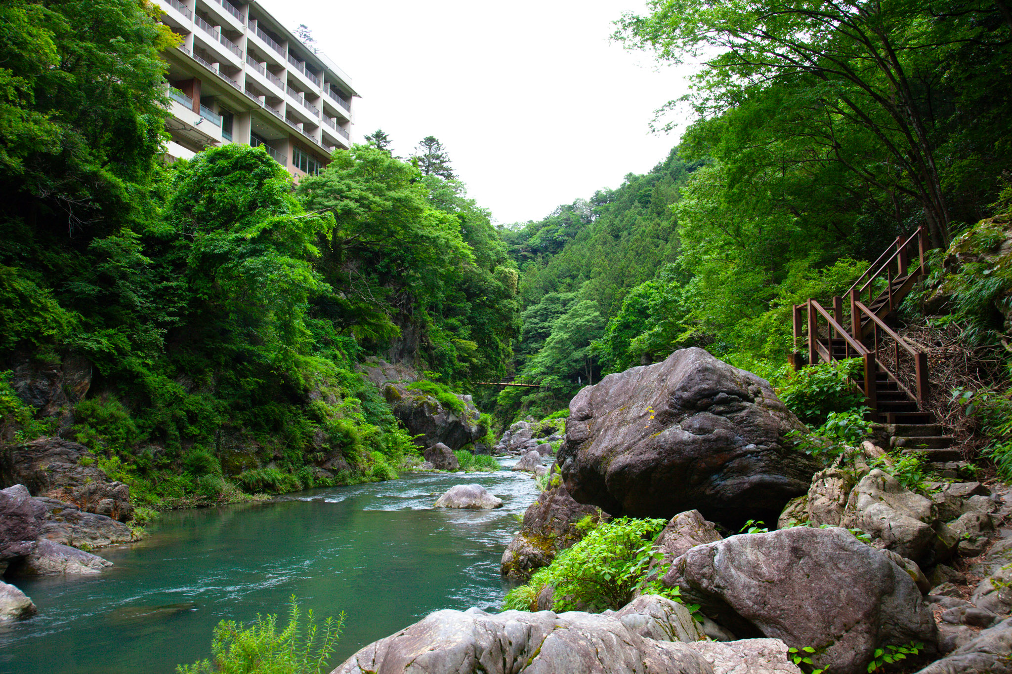 The Tama River below a riverside inn building, green water flowing past large boulders with a wooden staircase climbing the far bank