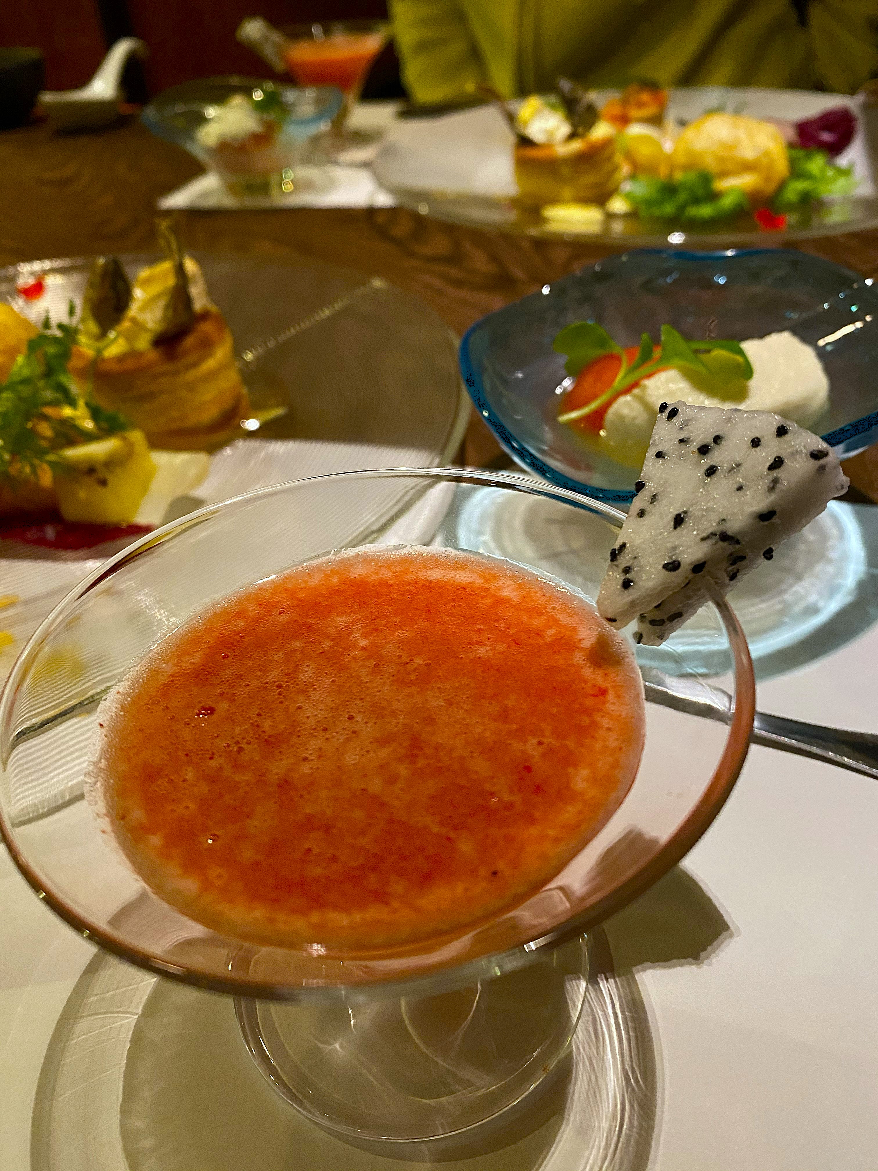 Opening courses of the kaiseki dinner at Satonoyu Waraku — in the foreground a footed glass bowl of tomato soup with foam, on a blue plate beside it a slice of dragon fruit with cream cheese and greens, elaborate appetizer plates visible behind