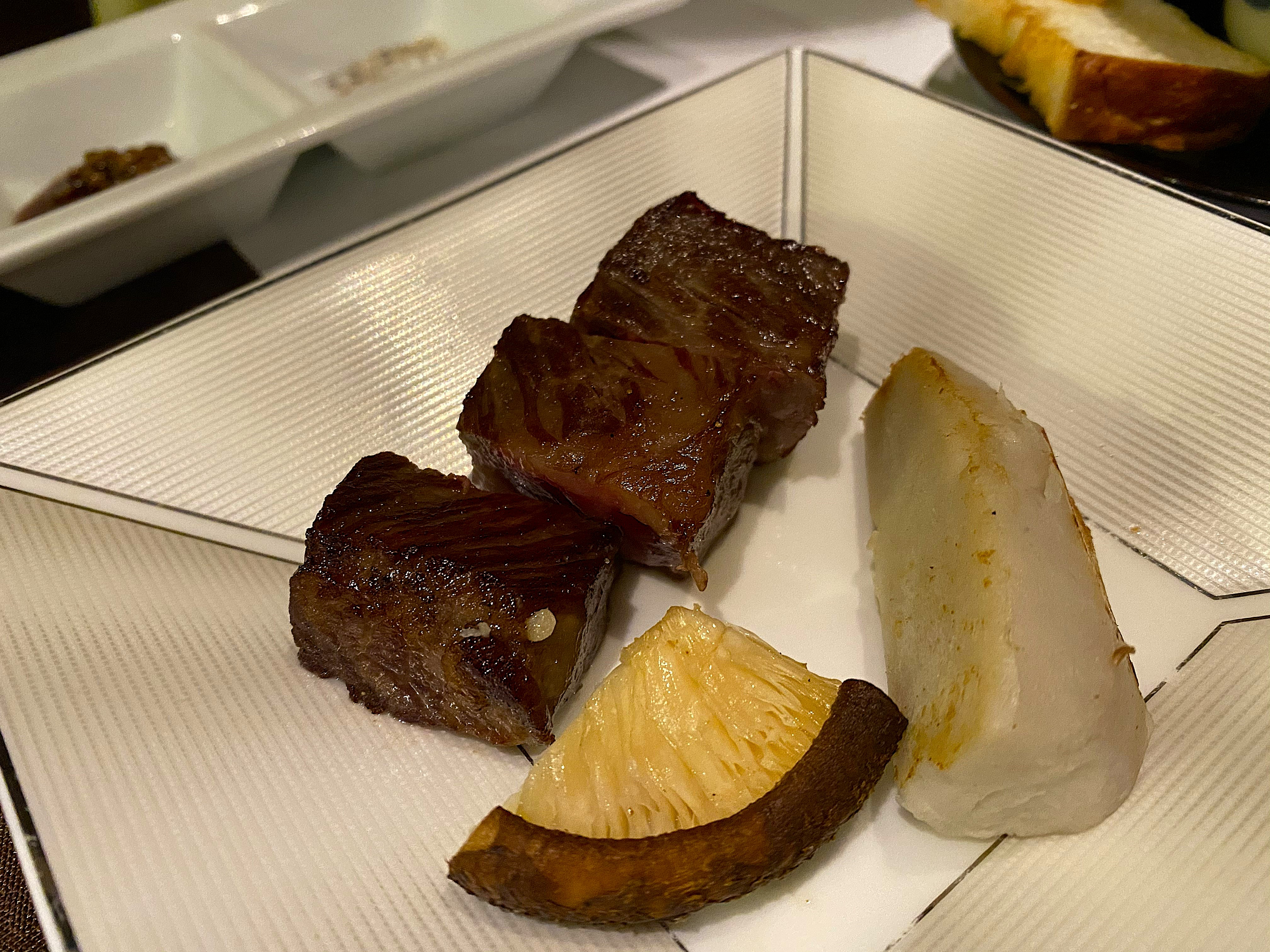 Grilled wagyu beef course at Satonoyu Waraku — cubes of deeply caramelized wagyu beef alongside roasted lotus root and turnip on a white square plate