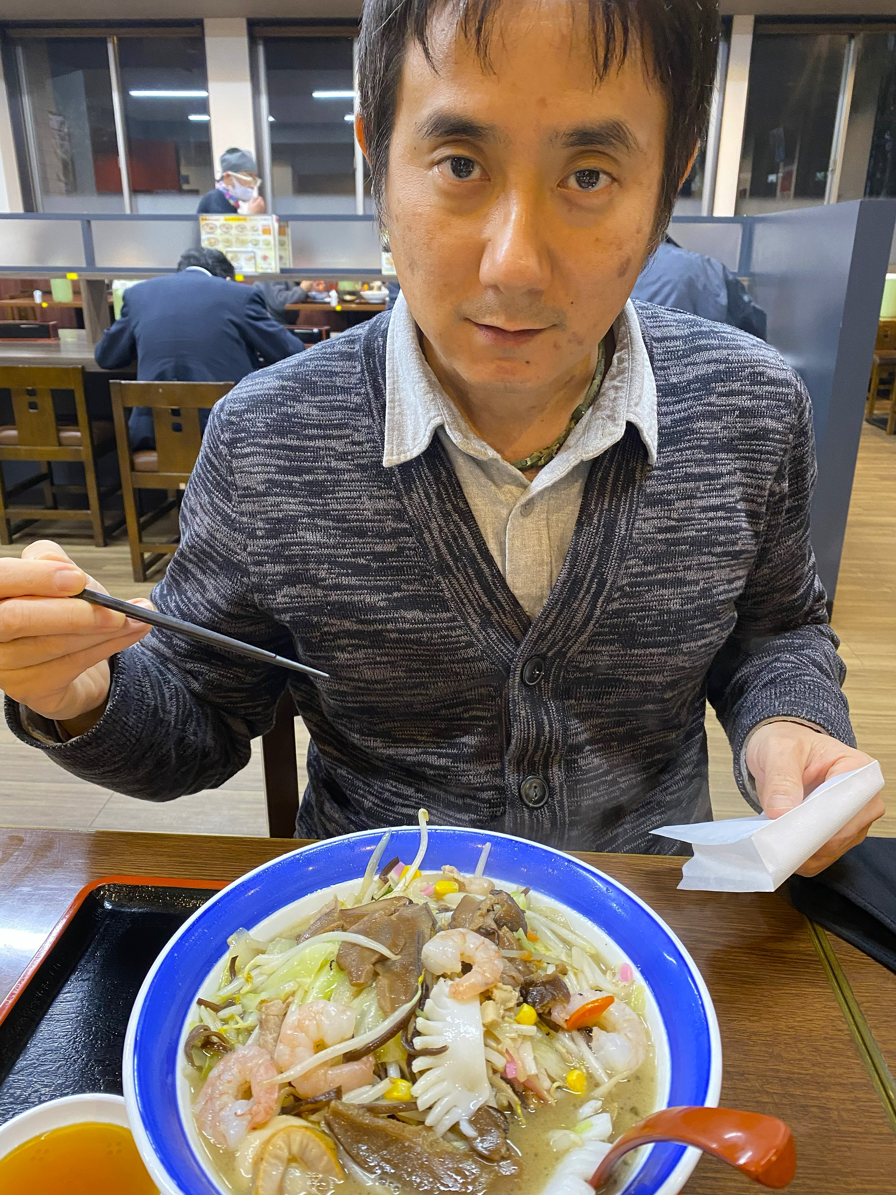 John sitting at the table at Chidori with a large blue-rimmed bowl of Imari champon in front of him — pork, shrimp, squid, mushrooms, cabbage and vegetables visible in the milky broth