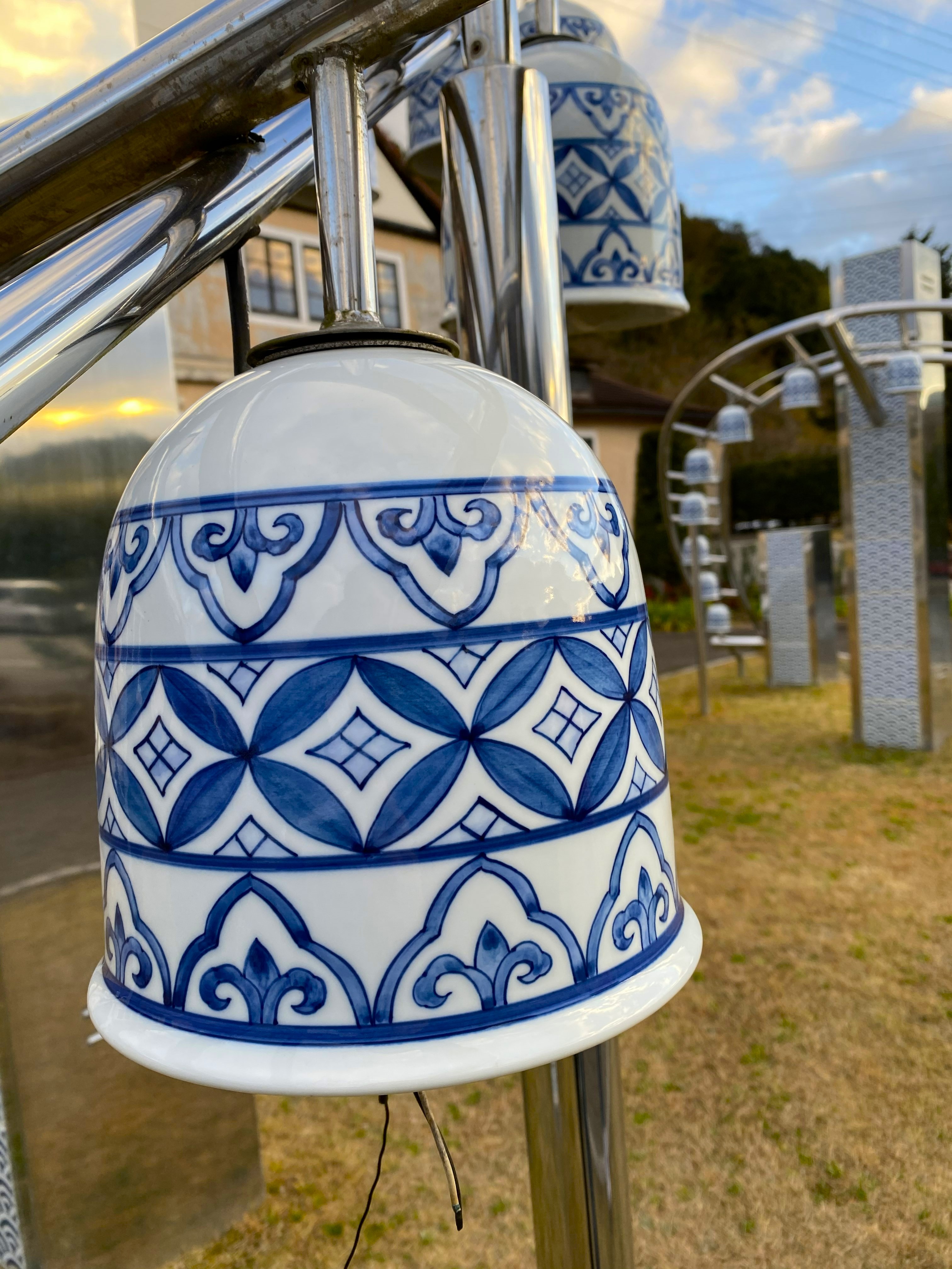 Close-up of a blue and white porcelain street lamp shade in Arita — hand-painted geometric and floral patterns in the classic Arita palette, more lamps visible on the arch behind it, the town and hills in the soft background