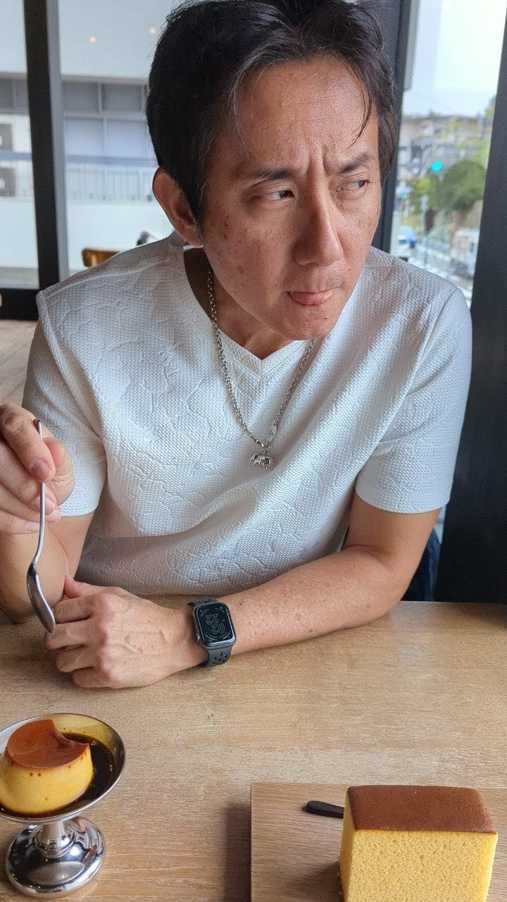 John eating the custard pudding at Shokado Kashiten — spoon in hand, Apple Watch visible, the castella still waiting on the board