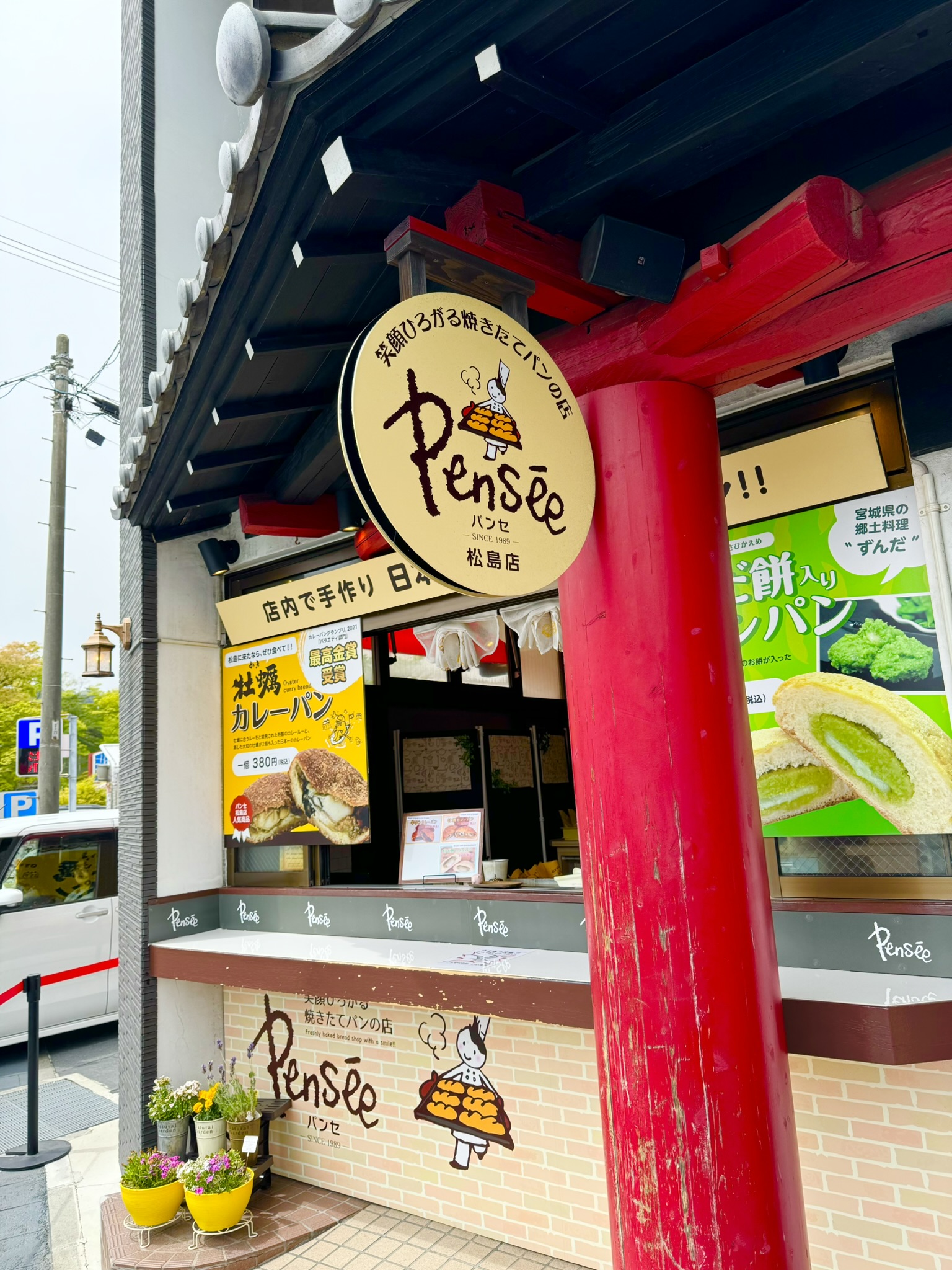 The Pensée bakery storefront in Matsushima — round wooden sign with the Pensée logo, red traditional pillars, and signage advertising the award-winning kaki curry bread