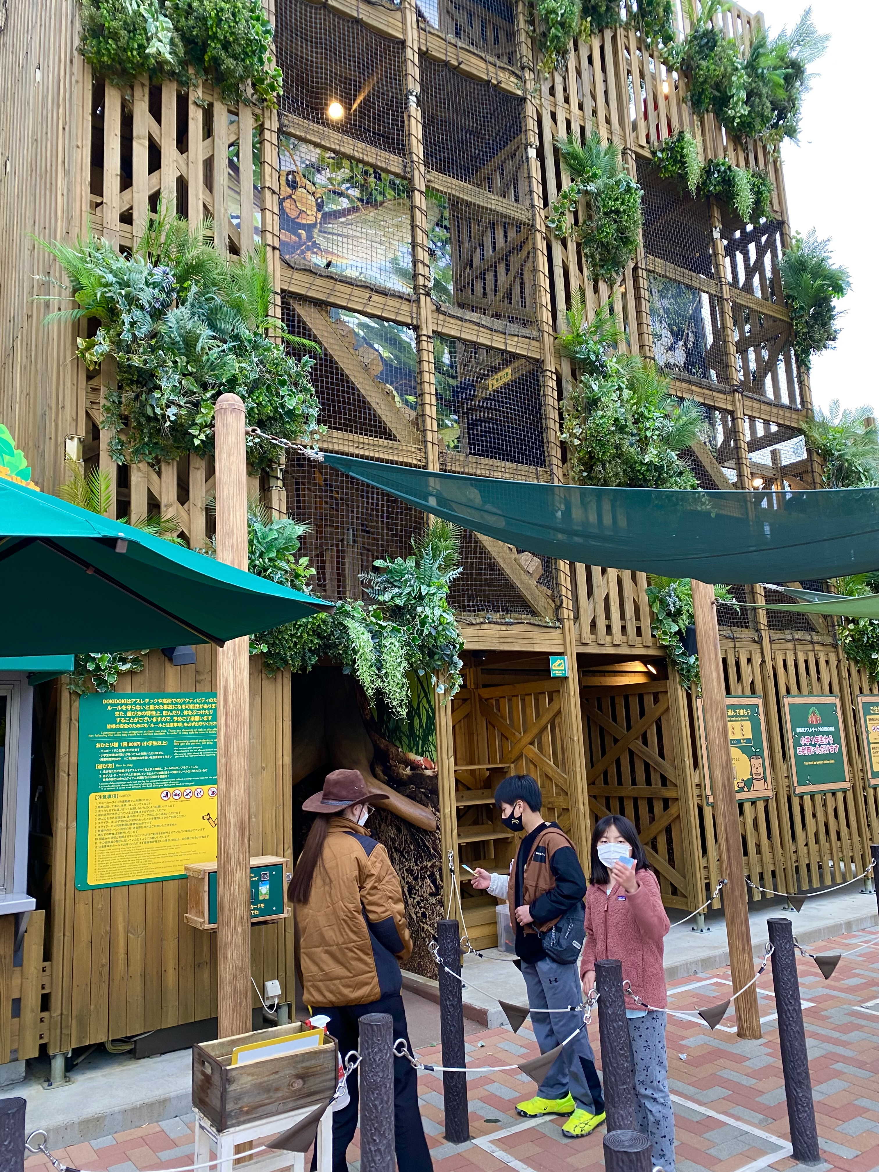 The multi-story Dokidoki athletic course wooden structure covered in tropical plants, with people visible climbing inside