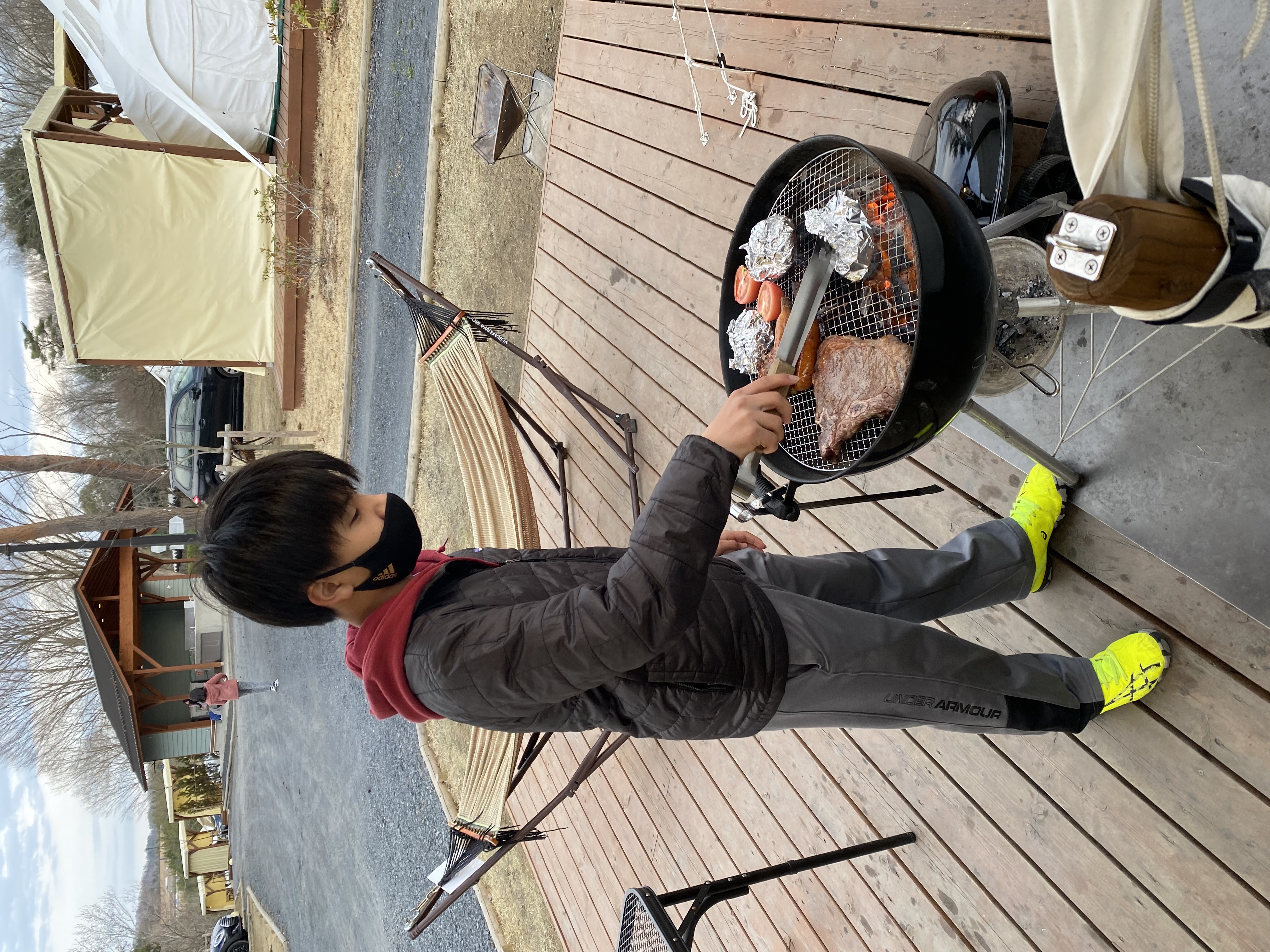 Jace grilling a large steak and vegetables on the Weber grill on the deck at the Motegi glamping site