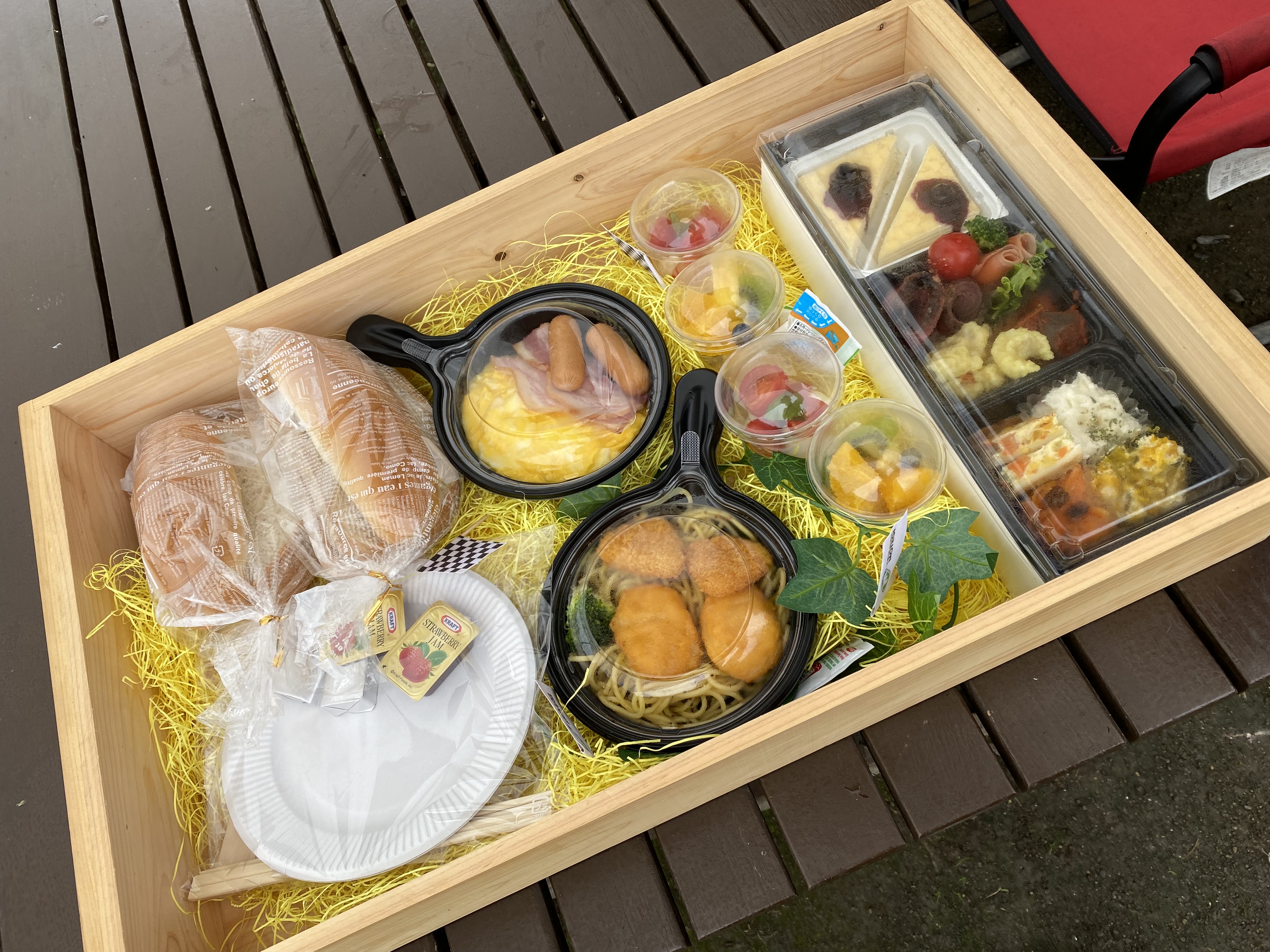 The glamping breakfast box in a wooden crate — eggs, sausages, pasta, bread rolls, fruit cups, and assorted sides all neatly presented