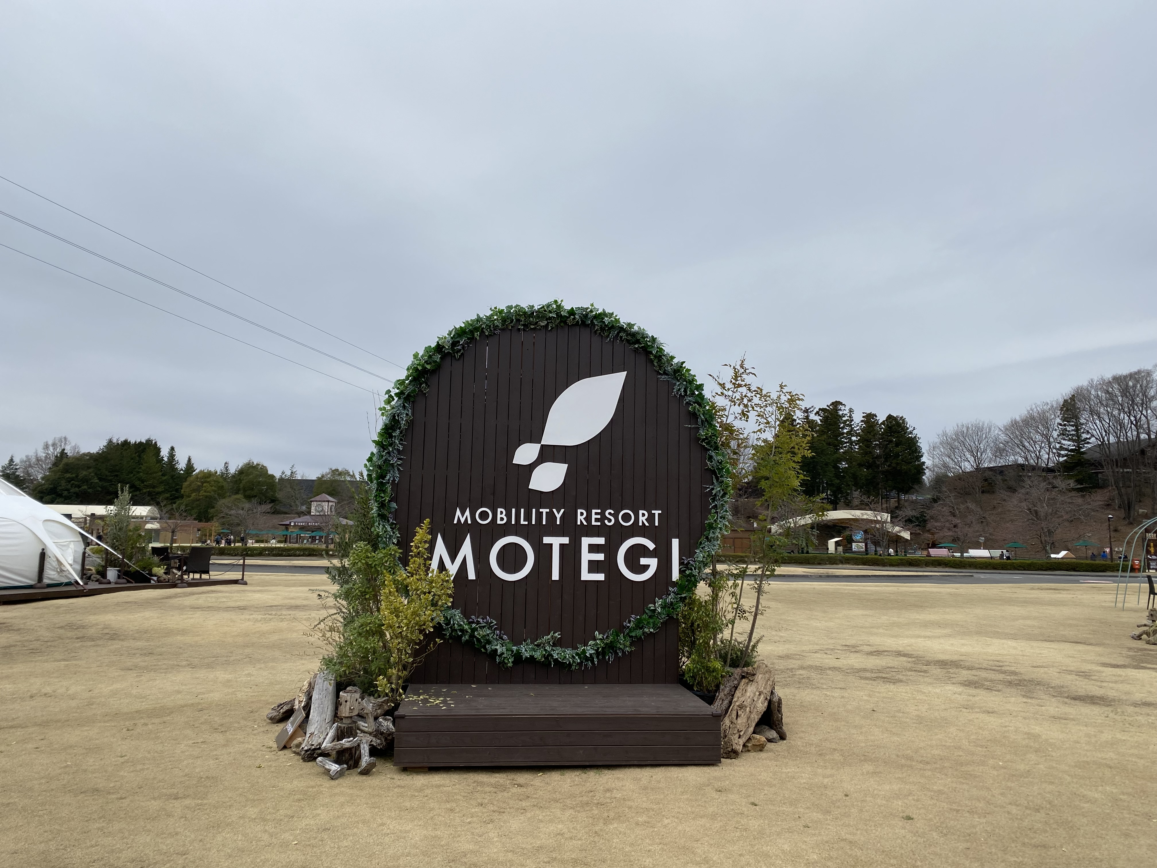 The circular dark wood Mobility Resort Motegi welcome sign surrounded by greenery
