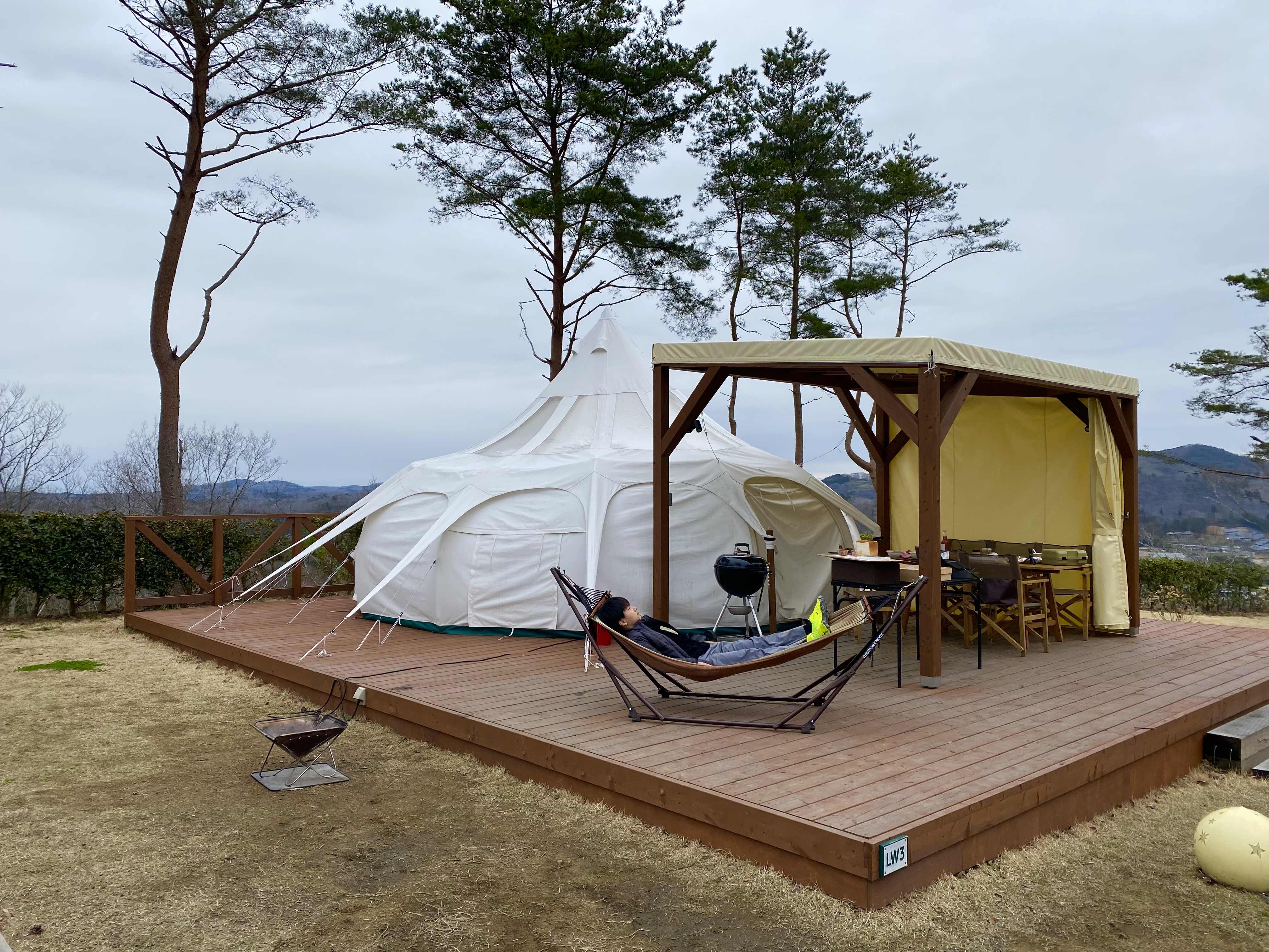 The lotus tent exterior during daytime — Jace relaxing in the hammock on the wooden deck with mountain views behind