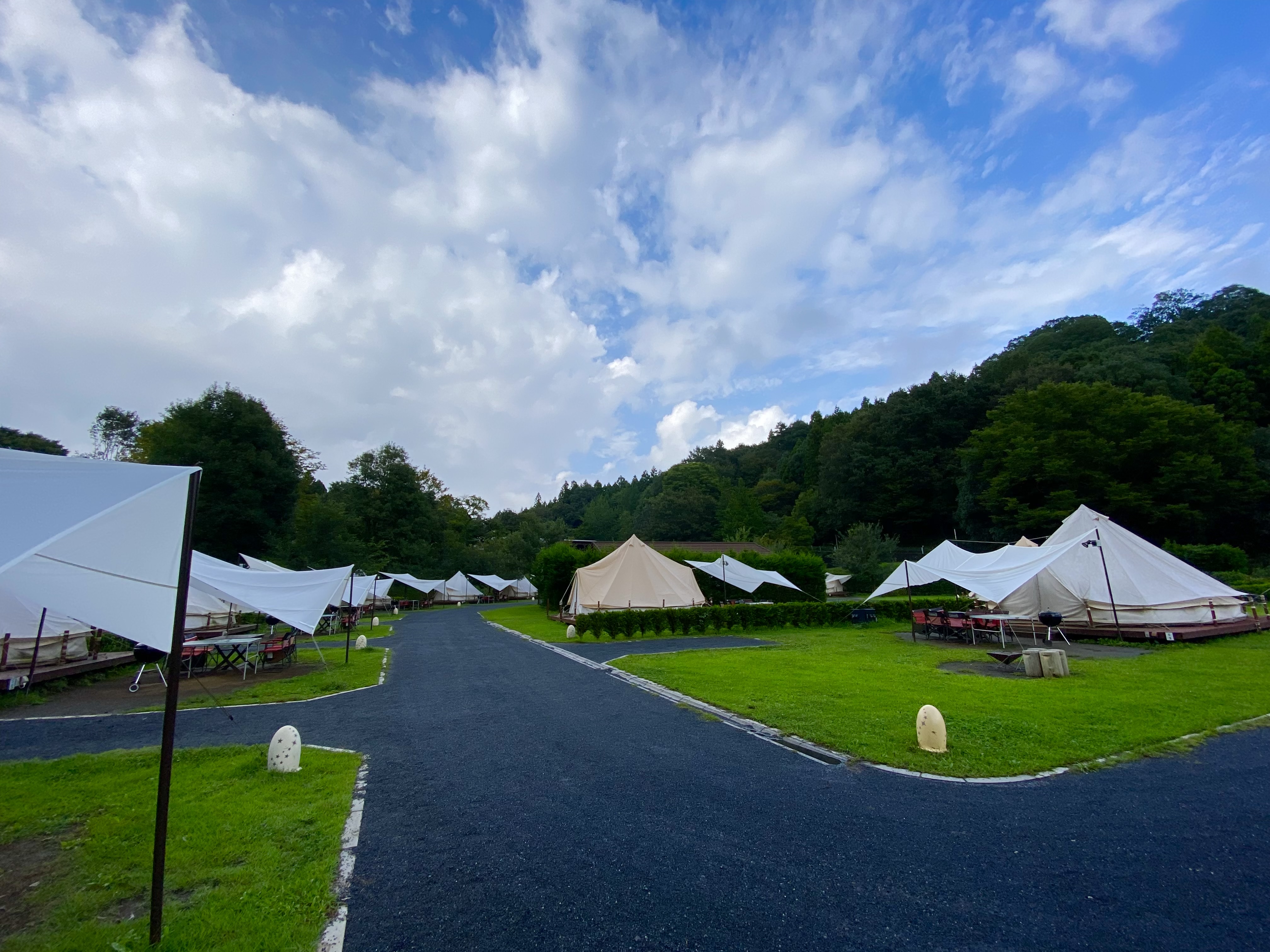 Wide view of the Motegi glamping area with rows of white tents lining the path under a dramatic blue sky with clouds