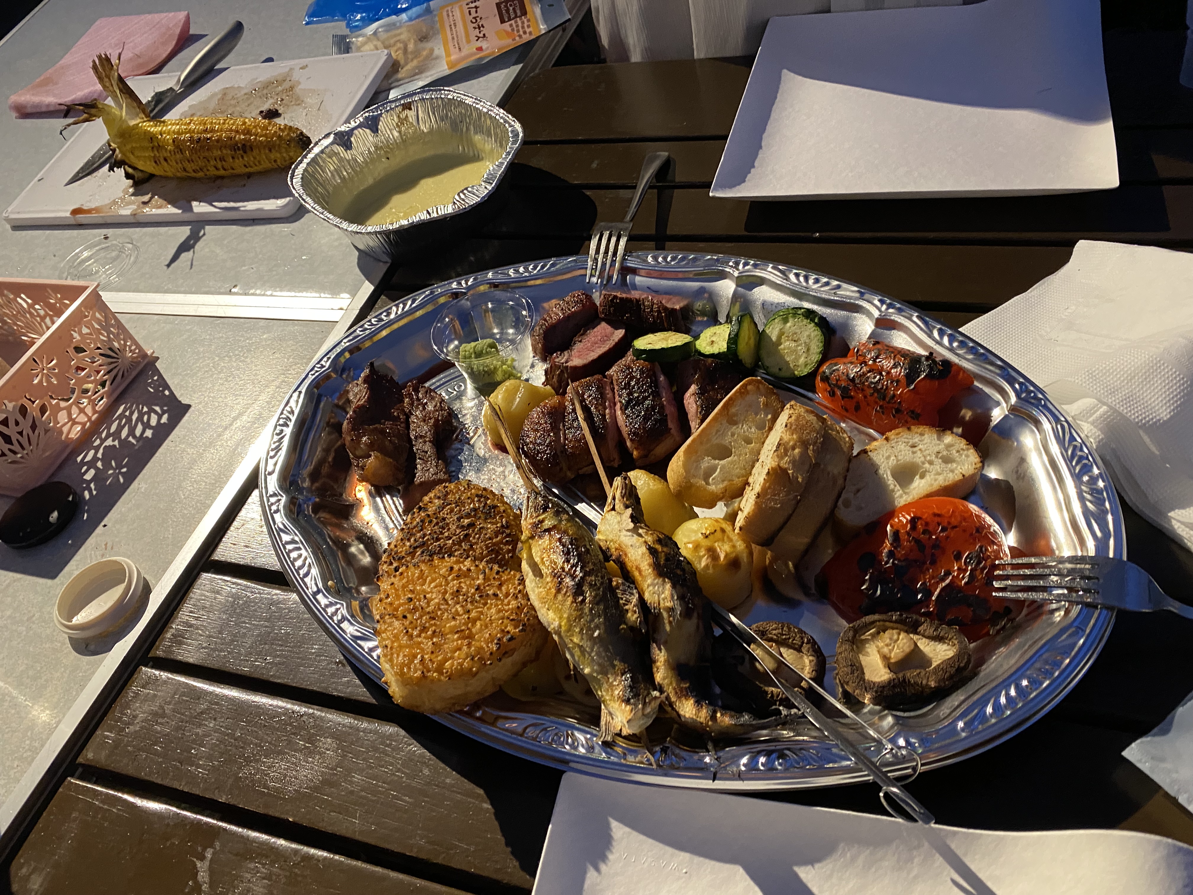 The full BBQ spread on a silver platter — steak, fish, corn, vegetables, mushrooms, bread all grilled together