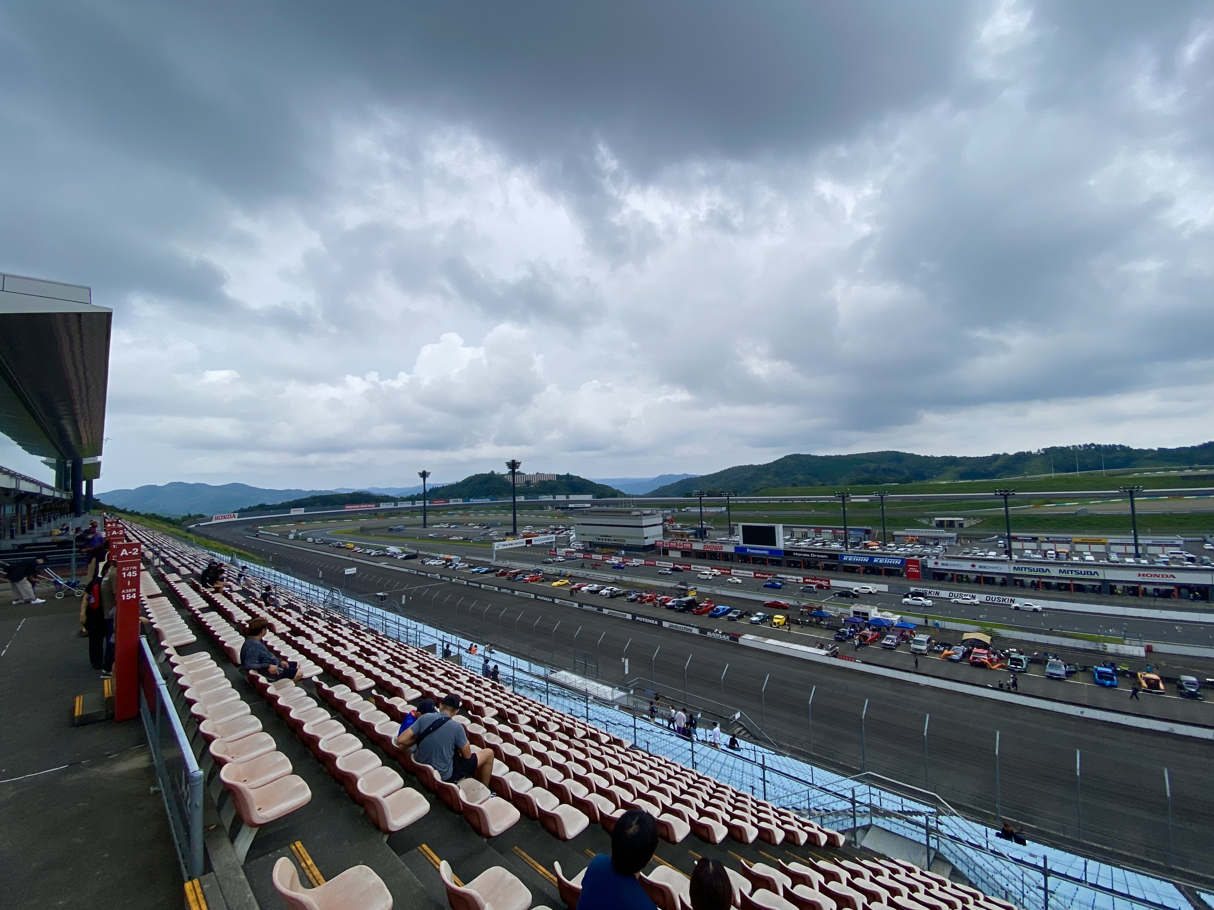 The Twin Ring Motegi main race track and grandstands from the spectator seating area, cars lined up on the straight with mountains beyond