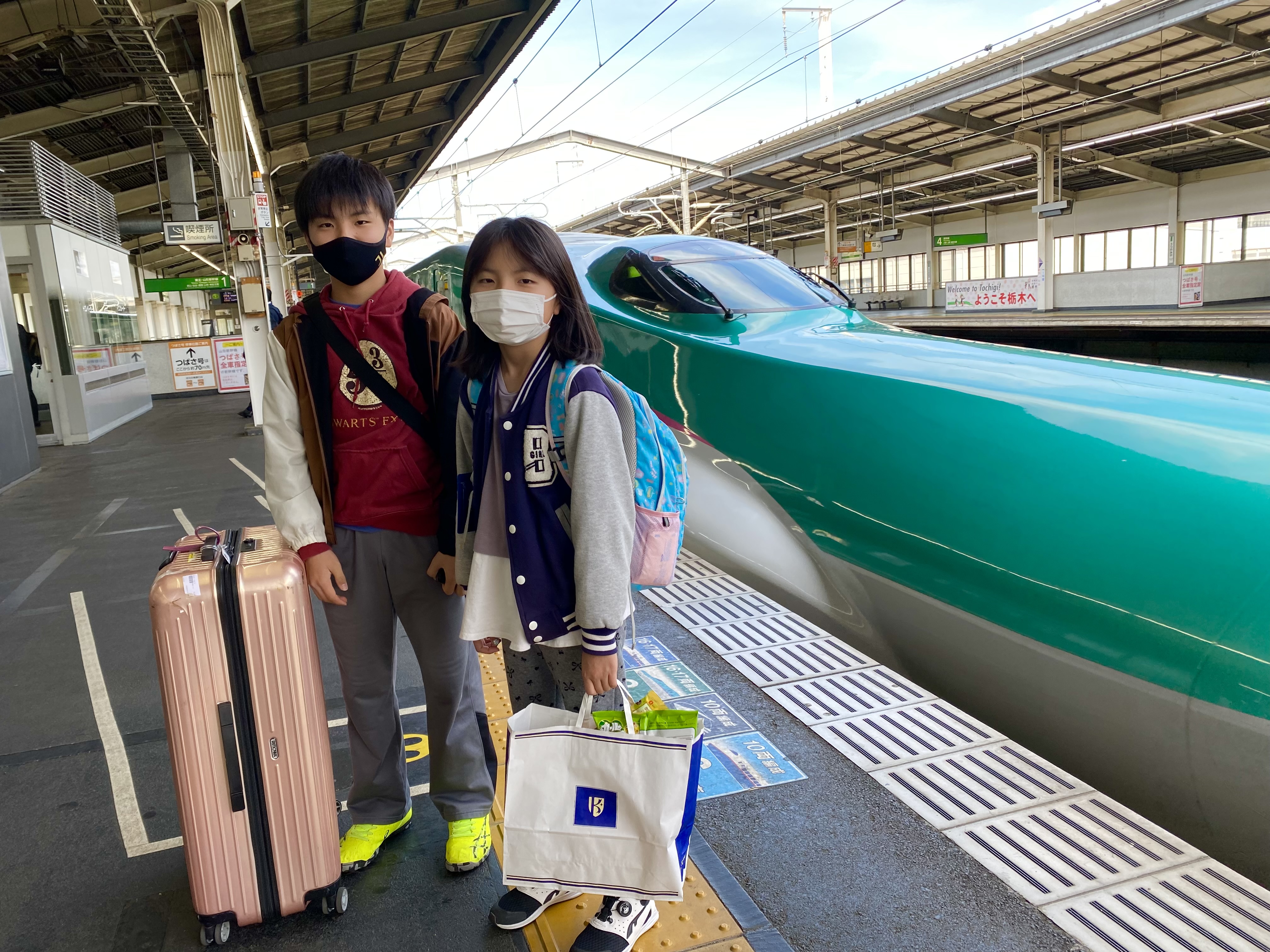 Jace and Maile standing on the Utsunomiya Shinkansen platform next to the green Hayabusa bullet train, luggage in hand