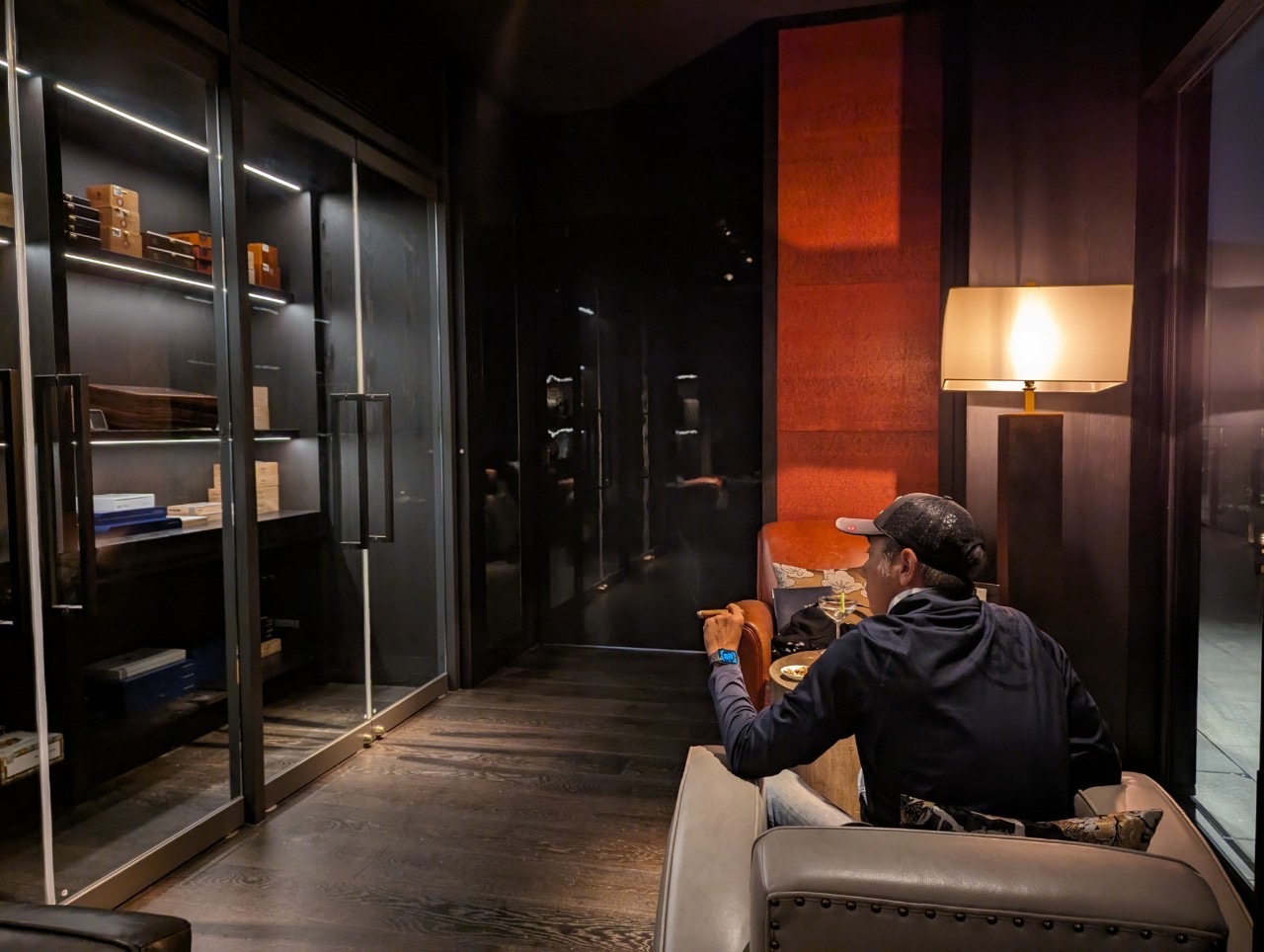 Park Hyatt Niseko cigar lounge interior — dark wood, illuminated humidor shelves, a man seated in a leather chair with a cigar, warm lamp light