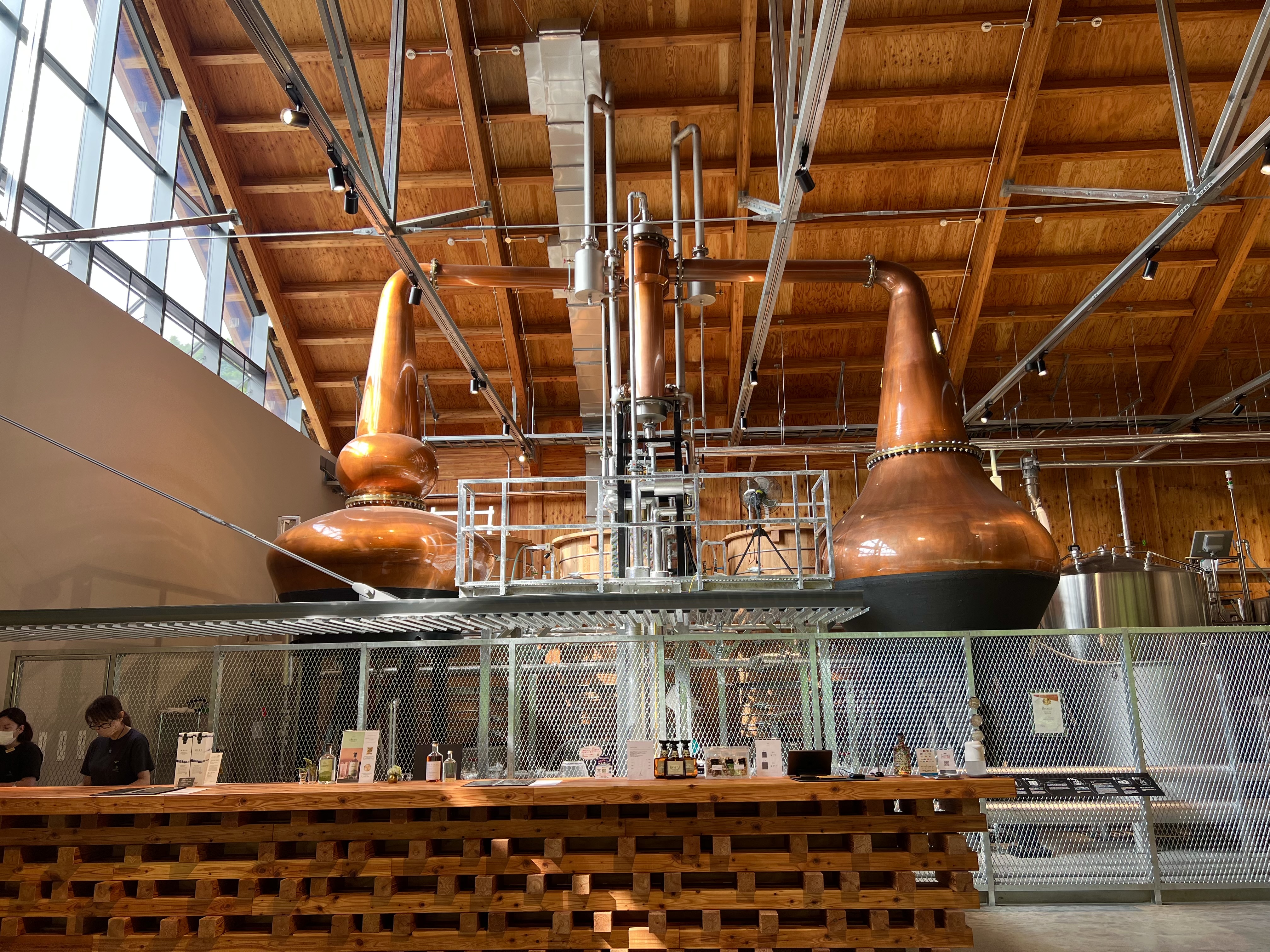 Inside Niseko Distillery — two large copper pot stills rising through the high wood-beamed ceiling, tasting bar below