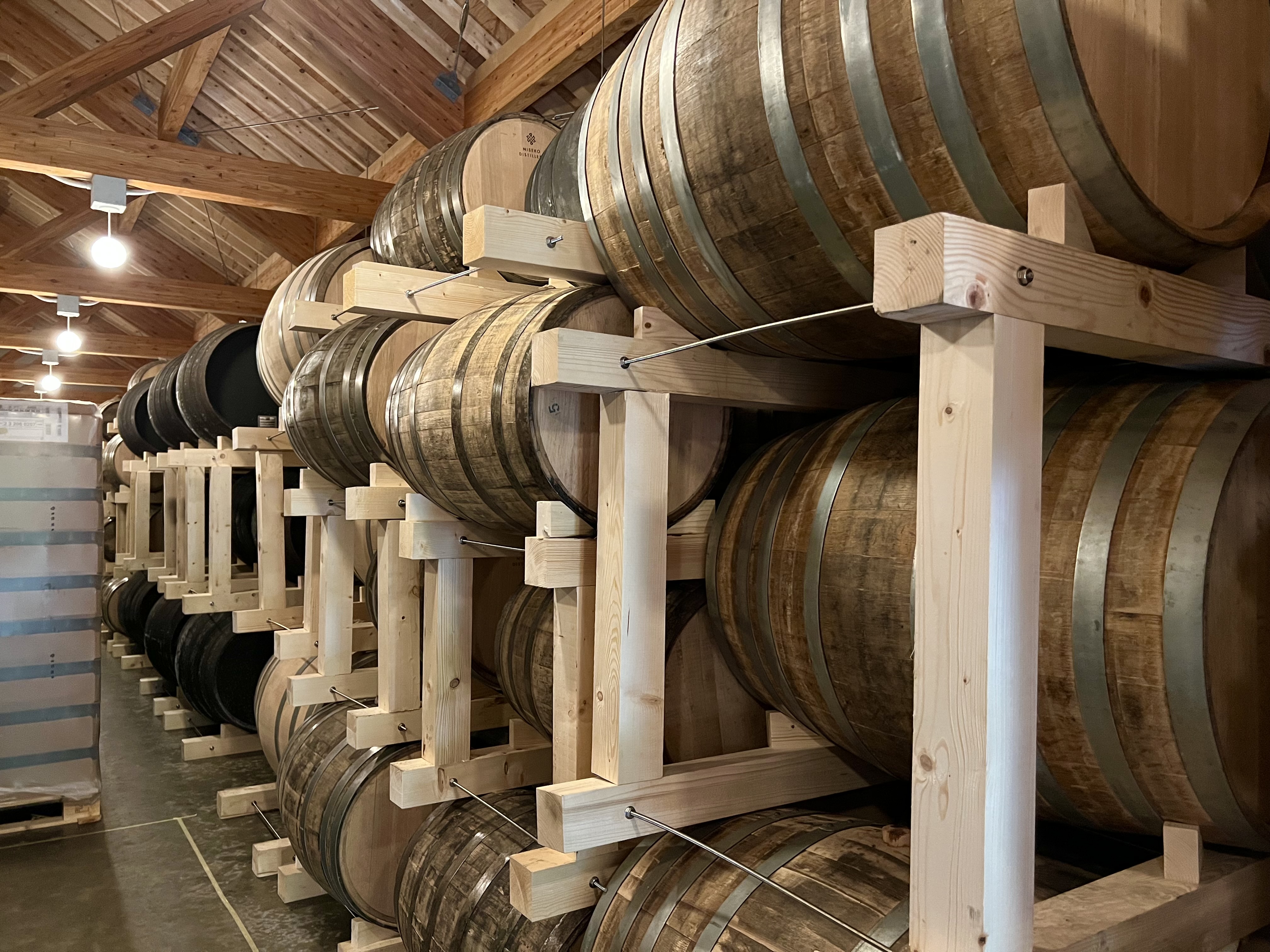 Barrel aging room at Niseko Distillery — rows of oak barrels stacked on wooden racks in a timber-framed warehouse