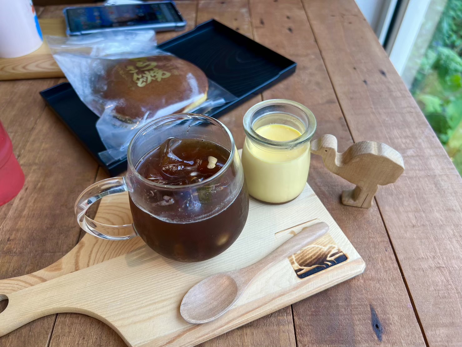 Ostrich farm café tray — iced coffee in a glass mug, fresh custard in a jar, and a wooden ostrich figurine on a wooden serving board