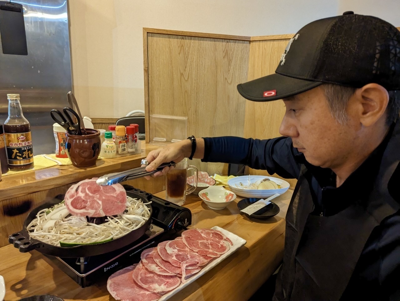 John working the Genghis Khan grill — lamb over bean sprouts, sauces lined up beside the iron dome