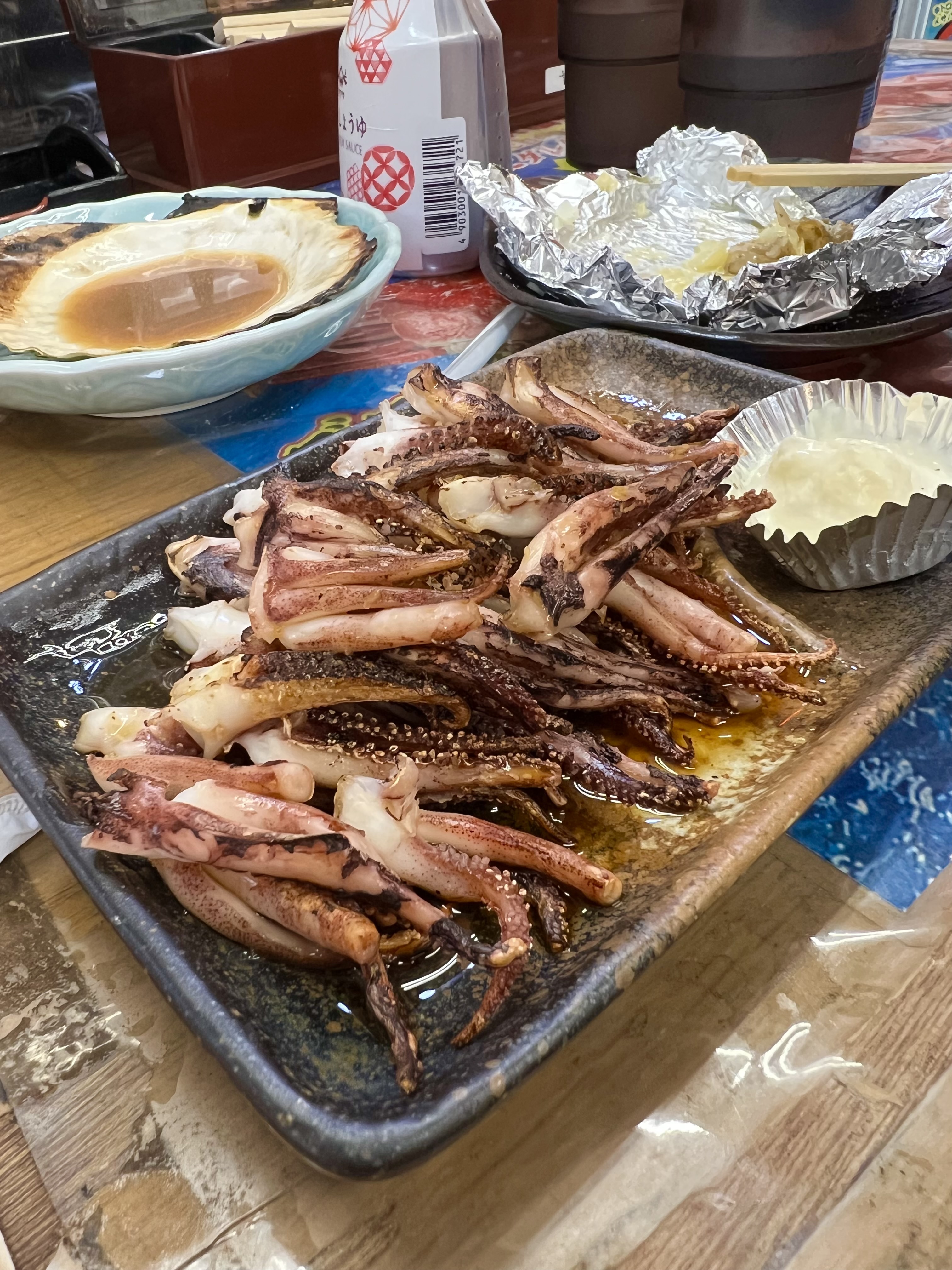 Grilled squid tentacles piled on a ceramic plate at an Otaru canal-side seafood stall, with a grilled scallop in the background