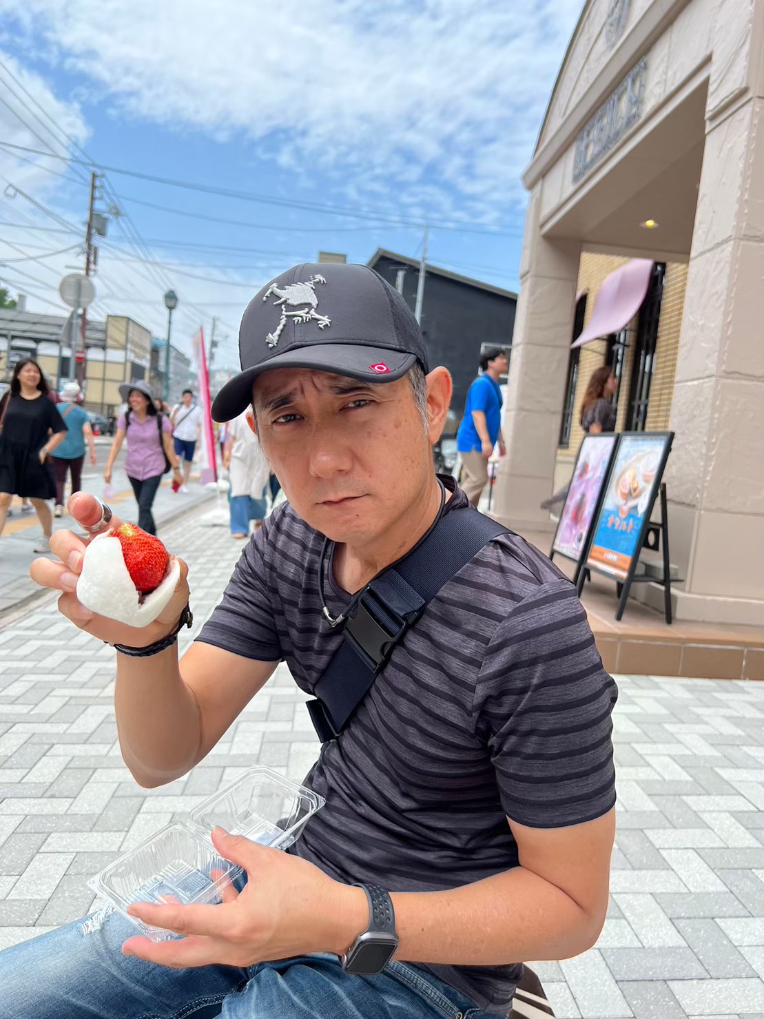 John holding a strawberry mochi — a large whole fresh strawberry wrapped in white mochi — outside on Sakaemachi street in Otaru