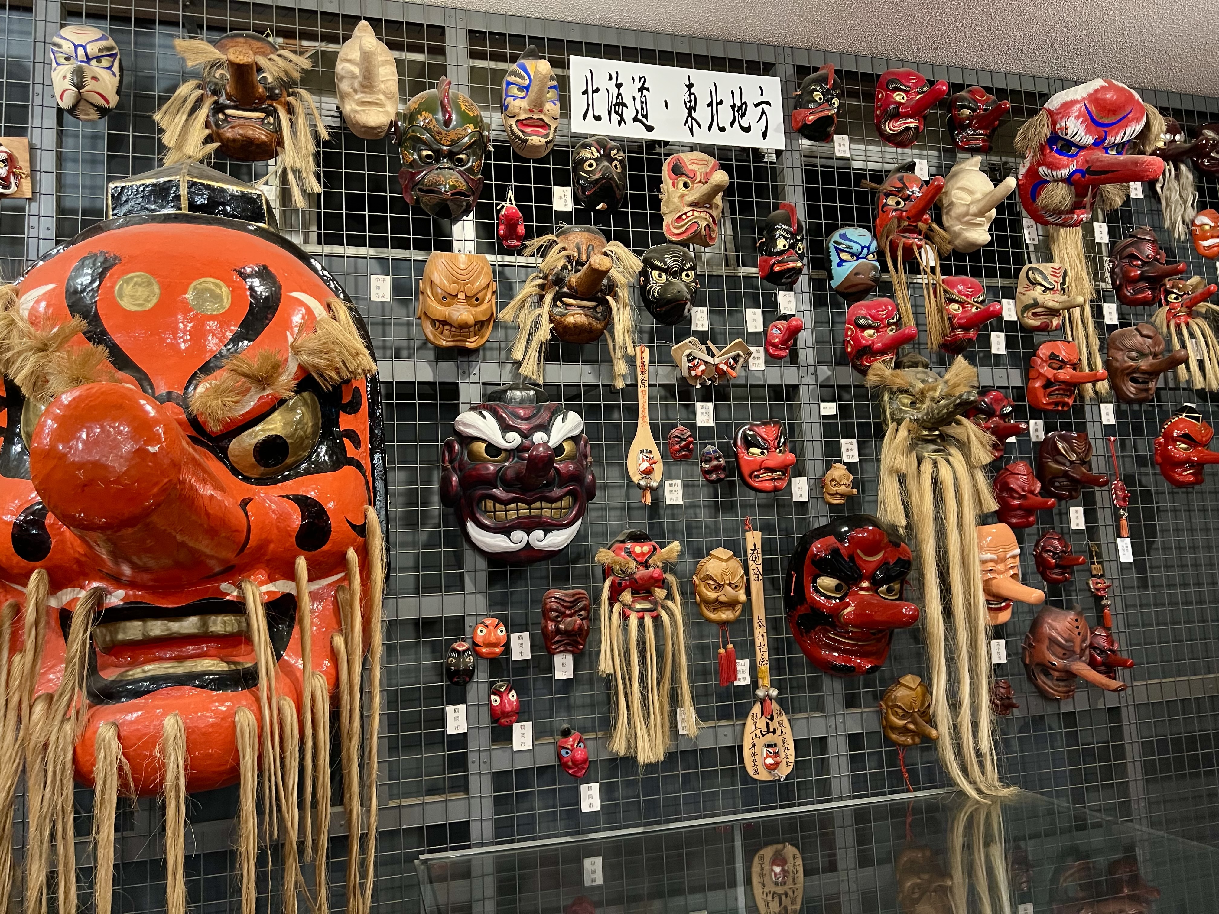 Wall of traditional Japanese tengu and oni festival masks at the Tengu Yama museum, labeled Hokkaido and Tohoku region