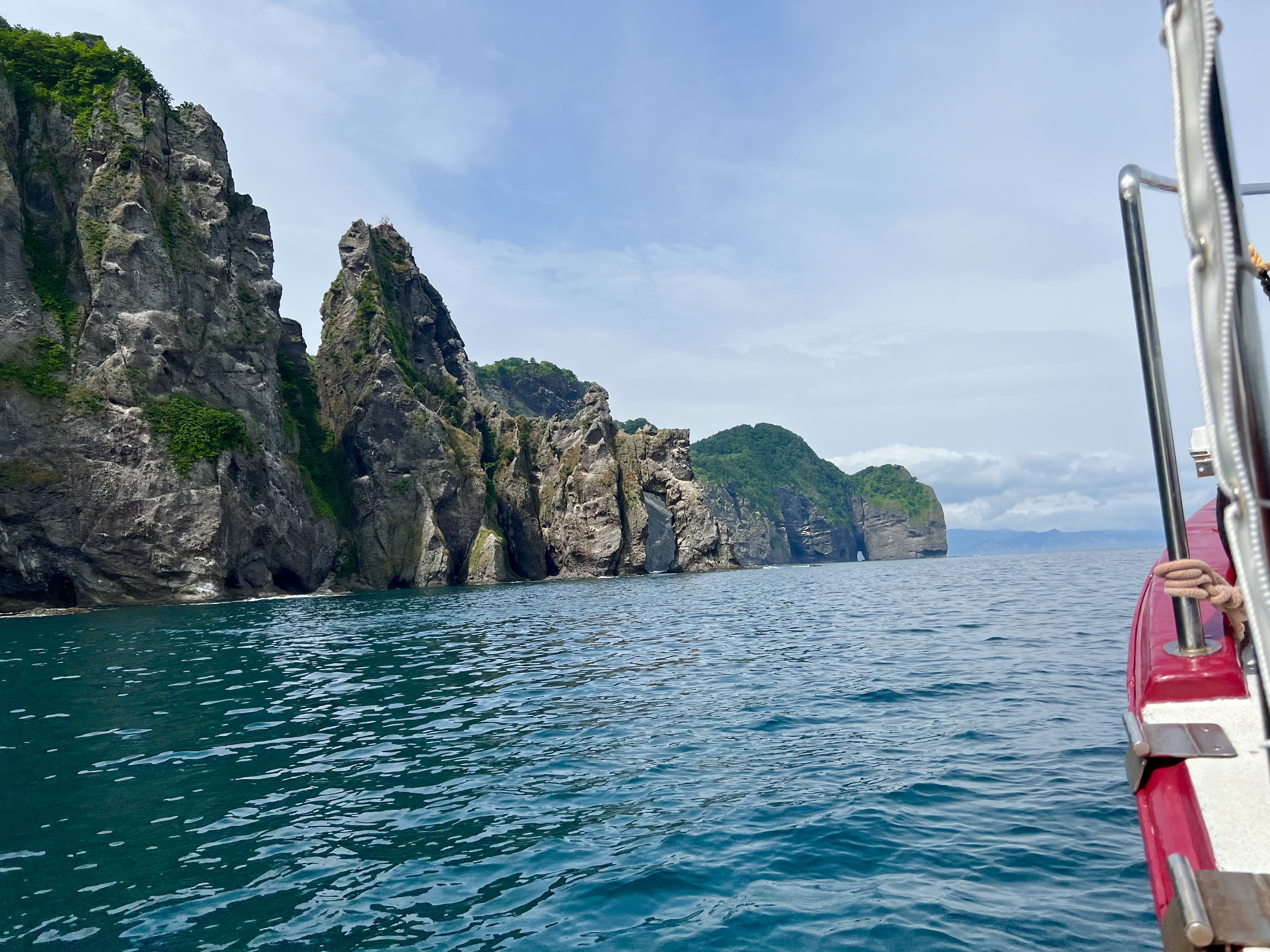 View from the cruise boat approaching tall volcanic sea cliffs along the Otaru coast, teal water, blue sky