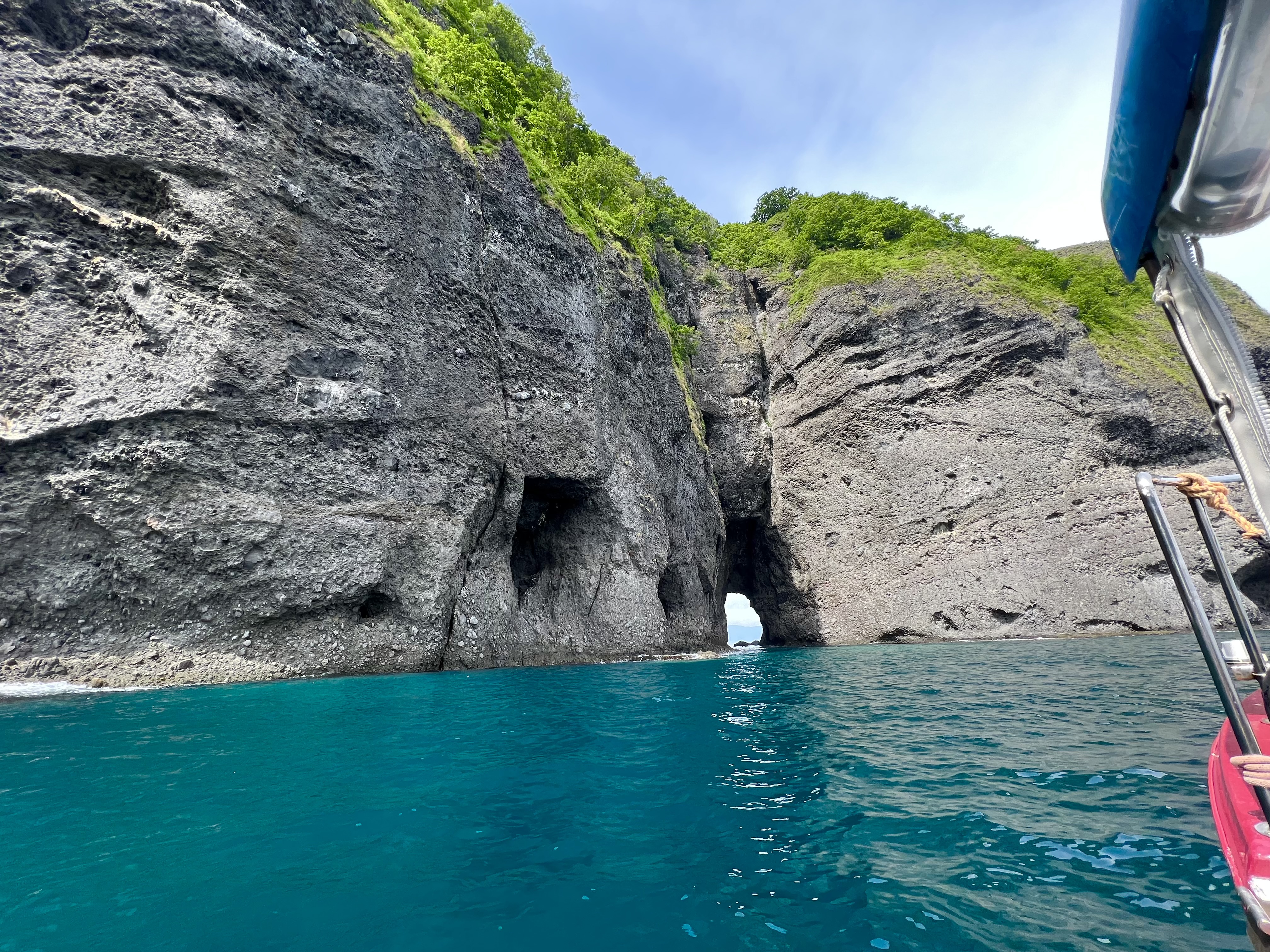 The boat approaching two cave openings carved into black volcanic rock, brilliant turquoise water in the foreground